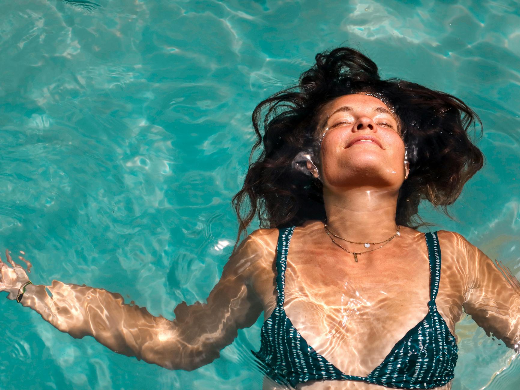 Kobieta po trzydziestce relaksuje się, unosząc na wodzie w słonecznym basenie