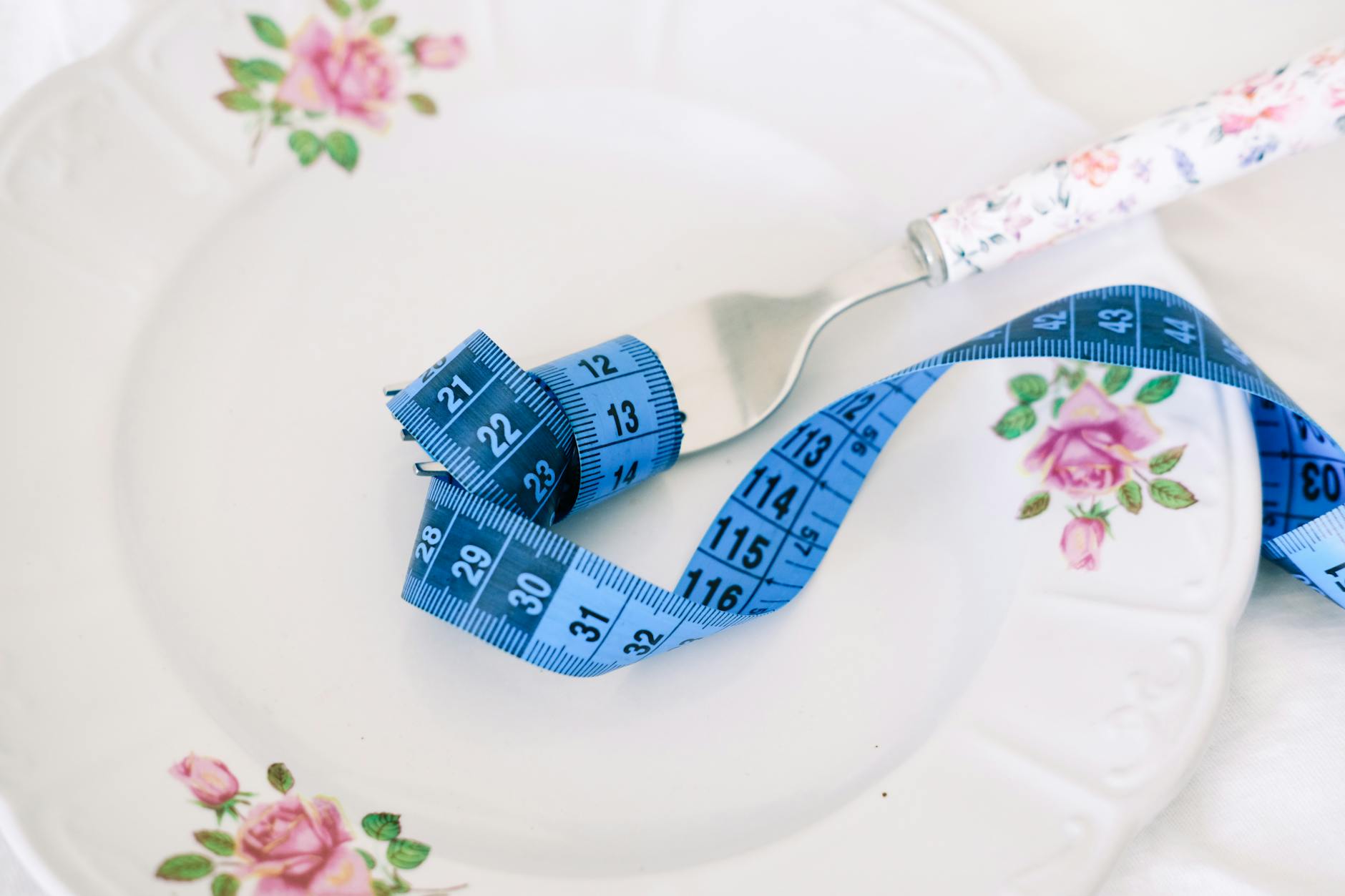 Talerz w kwiaty z widelcem i zwiniętą niebieską miarką nawiązujący do diety